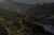 Aerial view of Sylvan Lake Lodge nestled among pine trees and granite rock formations in Custer State Park. The lodge sits near the shoreline of Sylvan Lake, with winding roads and forested hills in the background at sunset.